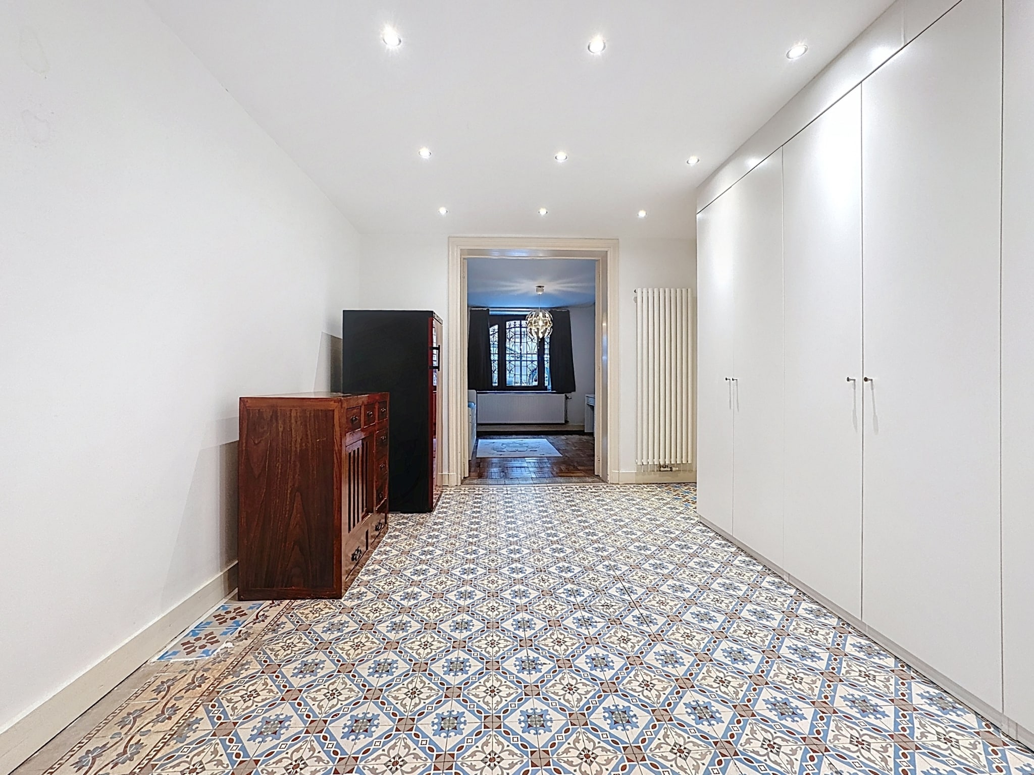 Hall moderne avec tuiles colorées, rangement élégant, et vue sur salon lumineux.