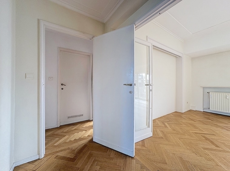 Hall lumineux avec parquet à chevrons, murs clairs, portes modernes et ambiance élégante.