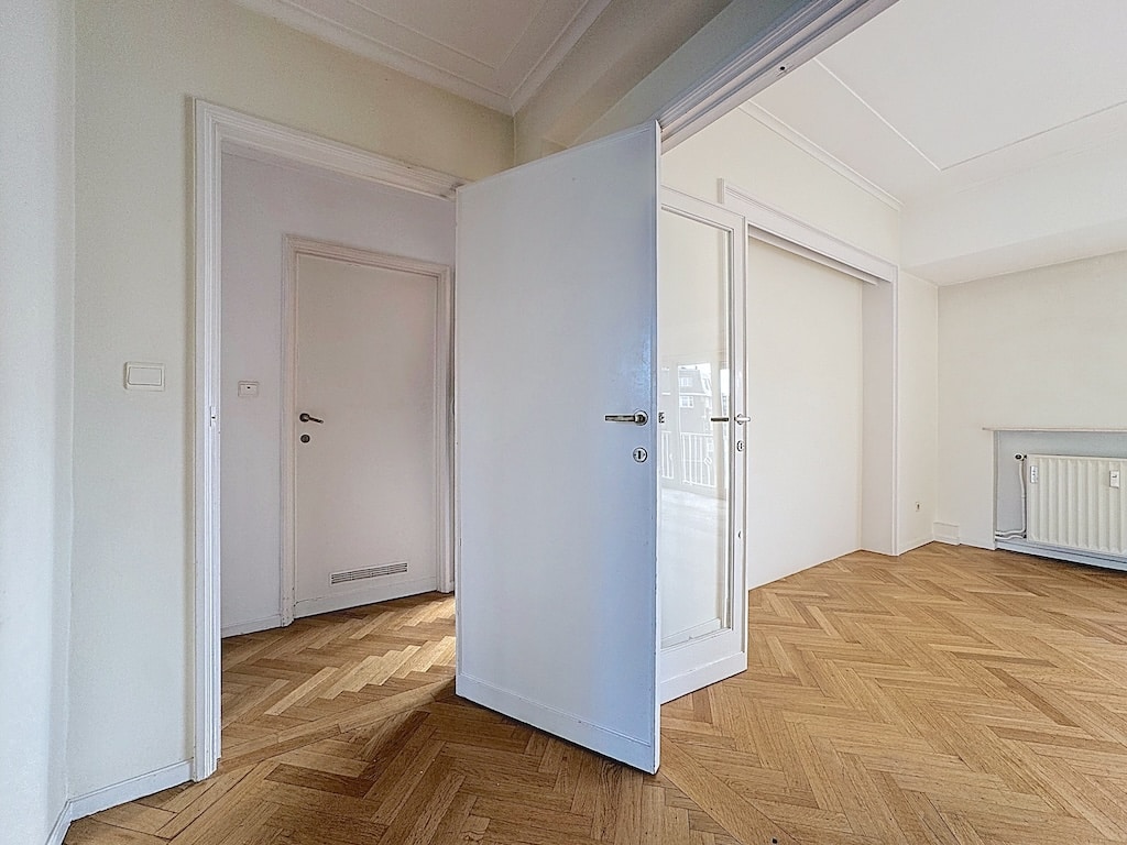 Hall lumineux avec parquet à chevrons, murs clairs, portes modernes et ambiance élégante.