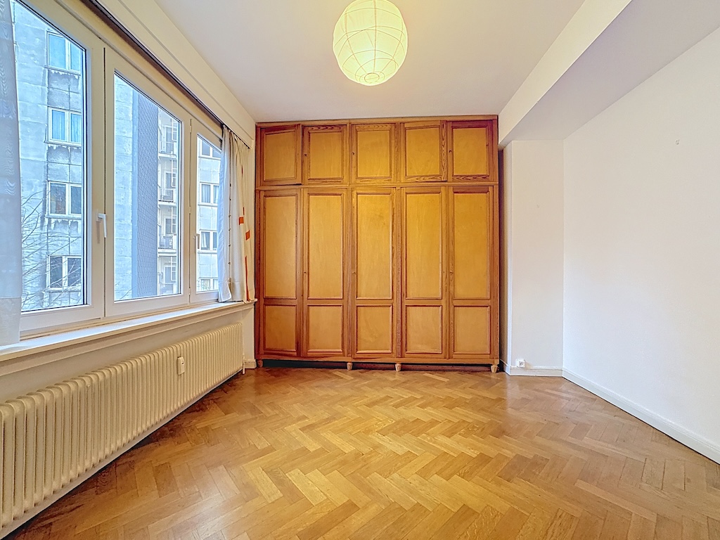 Salon lumineux avec parquet en chevron, grands fenêtres, rangement en bois moderne, ambiance chaleureuse.