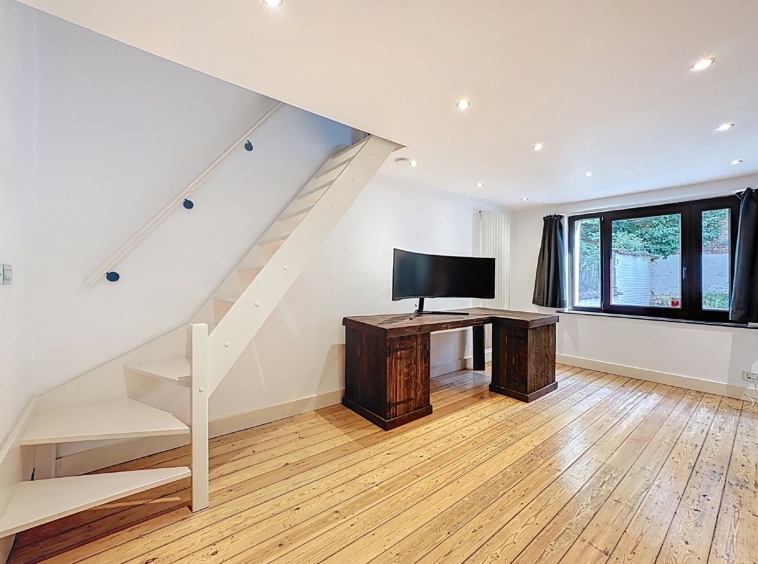 Intérieur moderne lumineux avec escalier spiralé coloré, bureau en bois sombre et grande télévision.