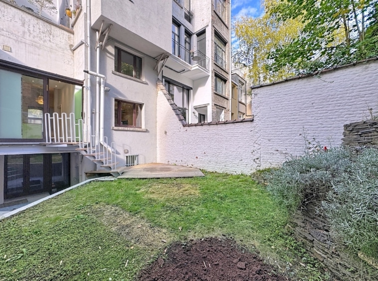 Jardin moderne avec terrasse pavée, pelouse verte, buissons et lumière naturelle.