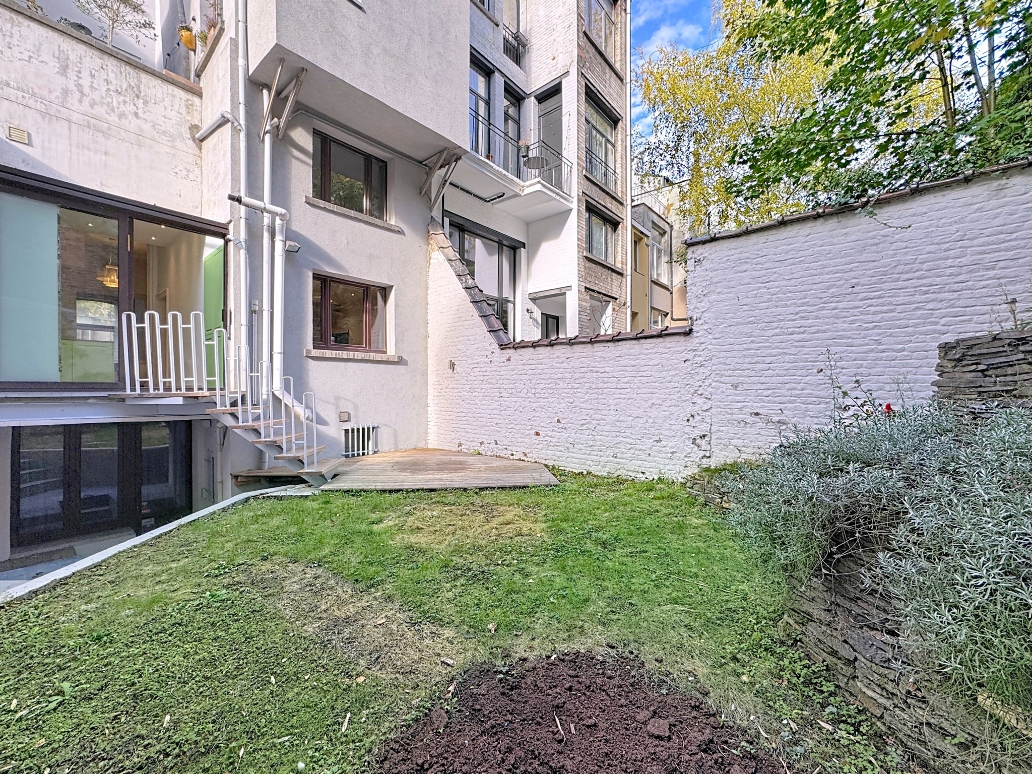 Jardin moderne avec terrasse pavée, pelouse verte, buissons et lumière naturelle.