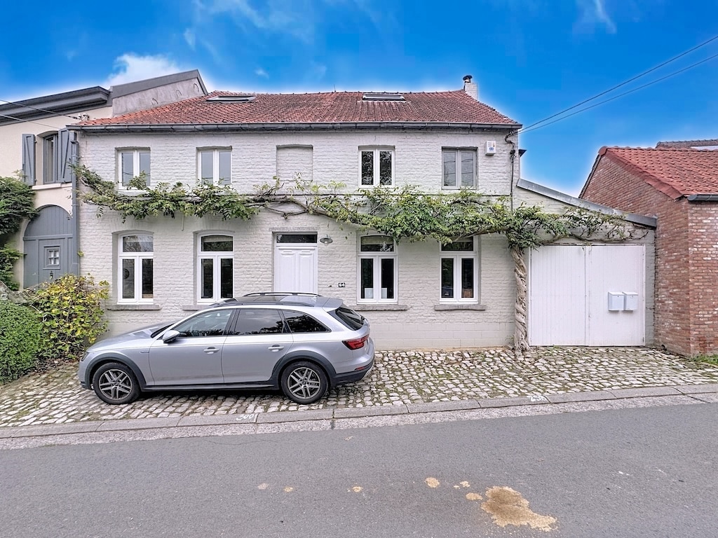 Rustiek huis met groene tuin, moderne auto, lichte gevel en harmonie tussen oud en eigentijds.