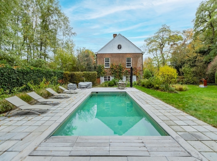 Piscine moderne avec jardin paisible et maison en briques, parfait pour la détente en extérieur.