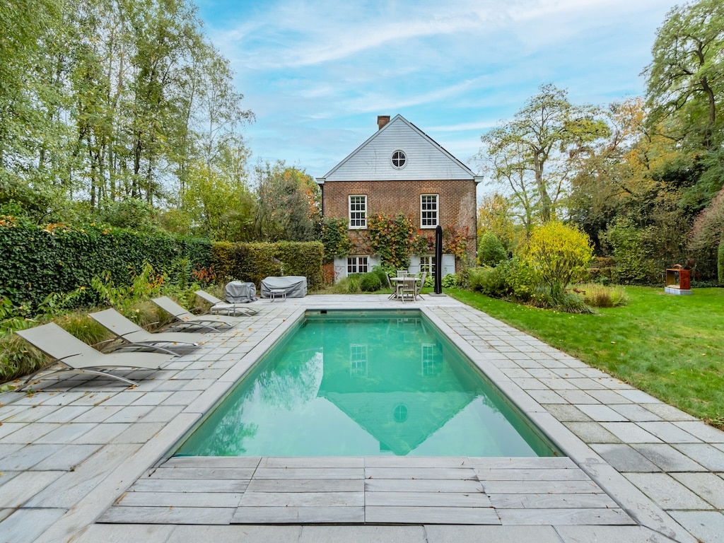 Piscine moderne avec jardin paisible et maison en briques, parfait pour la détente en extérieur.