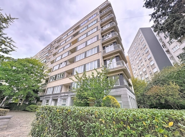 Immeuble résidentiel moderne avec grandes fenêtres, balcons, végétation luxuriante et ambiance paisible.