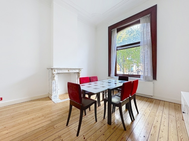Salle à manger moderne lumineuse avec chaises rouges, cheminée en marbre blanc et grande fenêtre élégante.