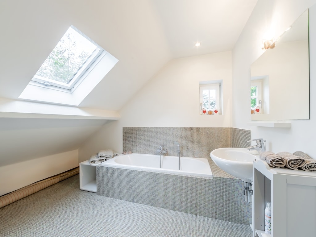 Salle de bain moderne minimaliste avec baignoire en pierre, lavabo sleek, lumière naturelle, ambiance sereine.