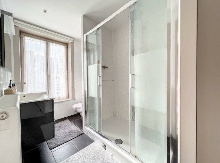 Salle de bain moderne avec douche en verre, lavabo noir brillant, grand miroir et lumière naturelle