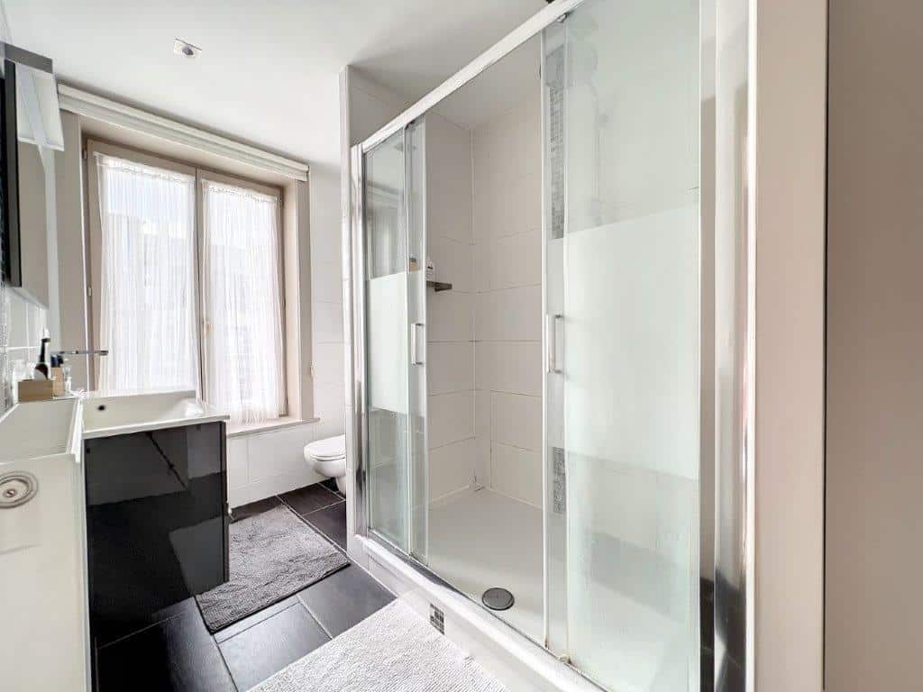 Salle de bain moderne avec douche en verre, lavabo noir brillant, grand miroir et lumière naturelle