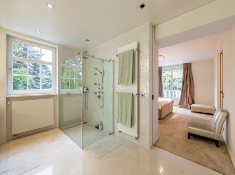 Salle de bain moderne attenante à une chambre lumineuse avec douche en verre et vue extérieure apaisante.