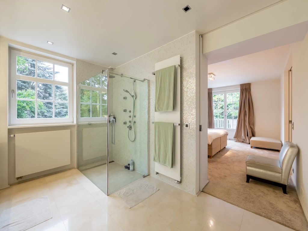 Salle de bain moderne attenante à une chambre lumineuse avec douche en verre et vue extérieure apaisante.