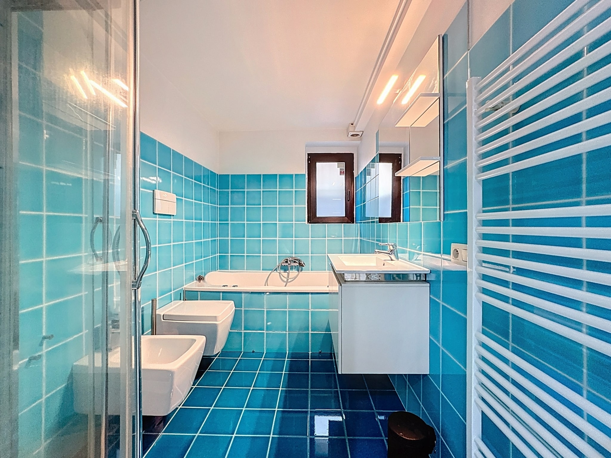 Salle de bain moderne en bleu clair avec douche, baignoire, lavabo et ambiance lumineuse.