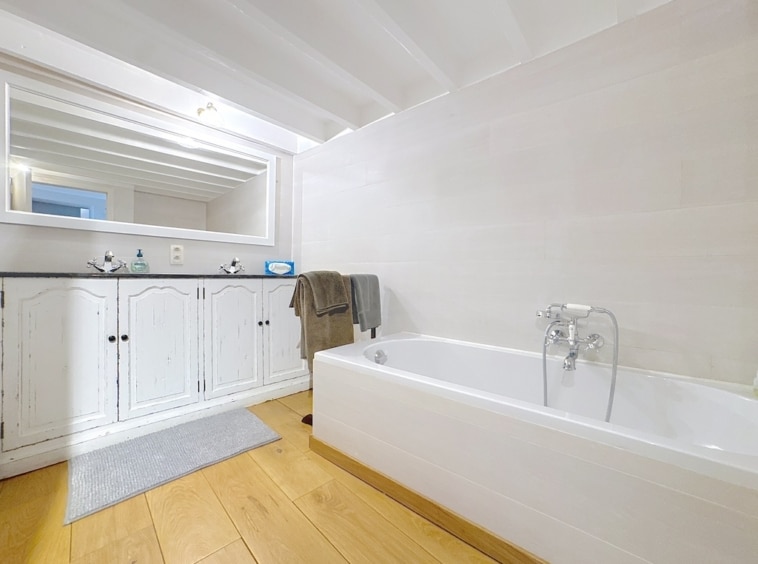 Lichte moderne badkamer met elegant bad, grote spiegel, houten meubels, ontspannen sfeer.