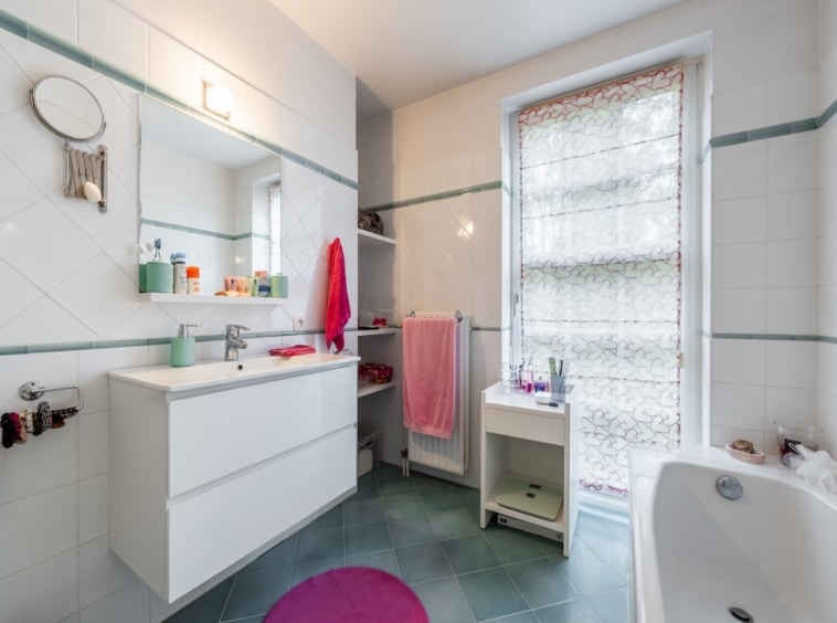 Salle de bain minimaliste lumineuse avec lavabo, baignoire, serviettes colorées et lumière naturelle.