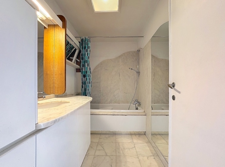 Salle de bain minimaliste avec baignoire en marbre, lavabo moderne, accents en bois et rideau bleu et blanc.