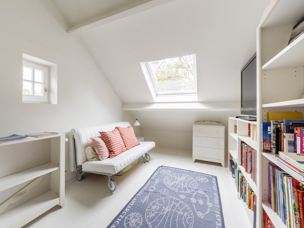 Salon lumineux et minimaliste avec canapé blanc, bibliothèque moderne, tapis bleu et grande lucarne