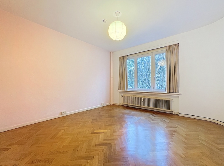 Salon lumineux minimaliste avec murs roses, parquet en chevrons, grandes fenêtres et ambiance chaleureuse.