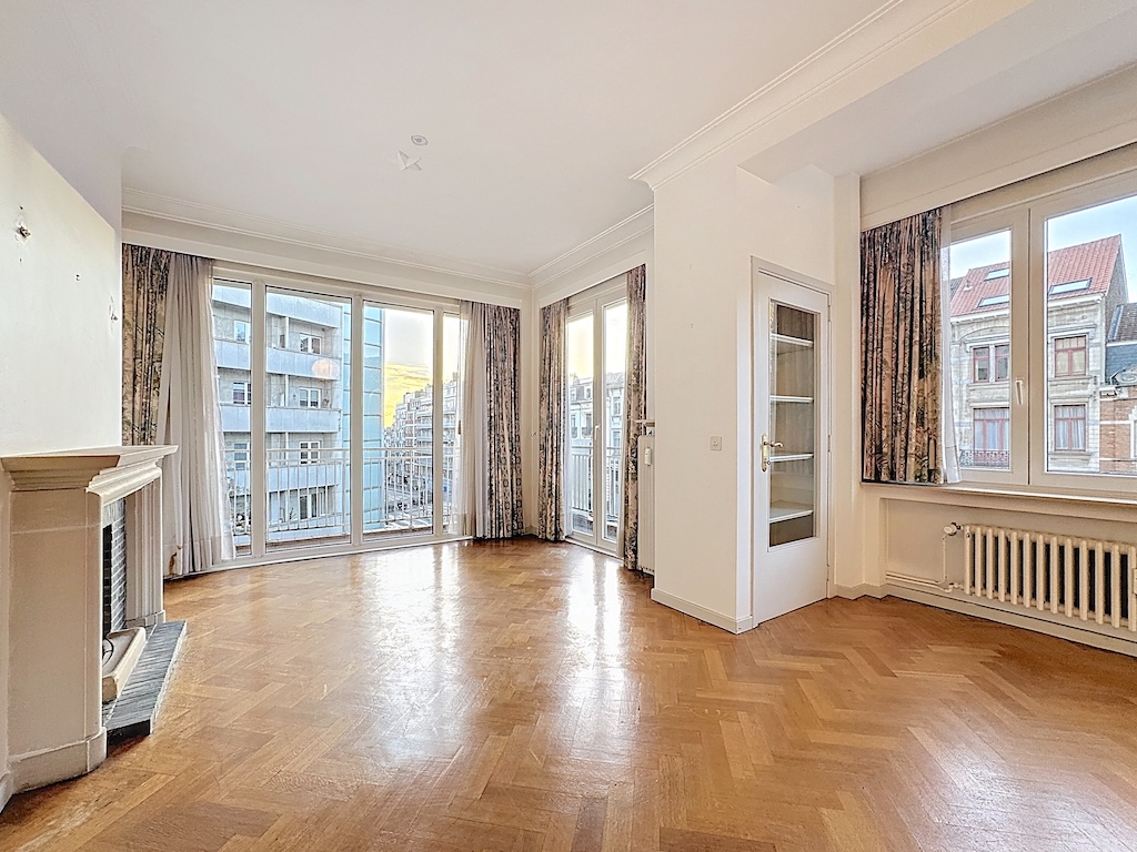 Salon lumineux avec cheminée, grandes fenêtres, parquet en chevrons et décoration élégante.