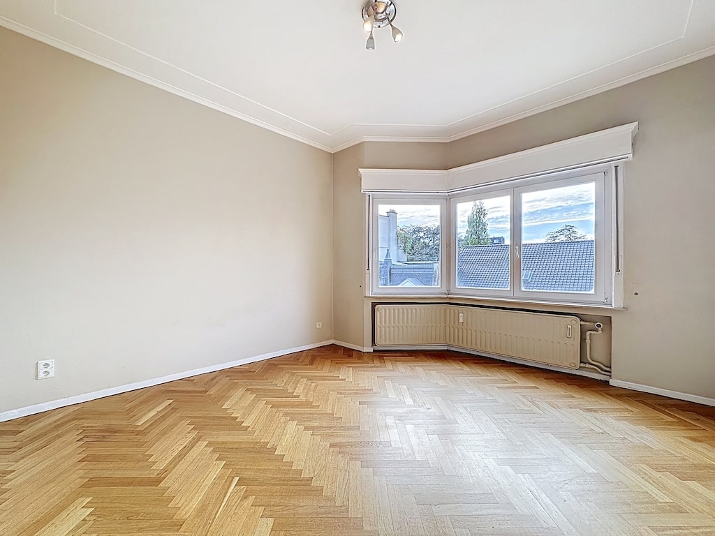 Salon lumineux avec grande baie vitrée, parquet en chevrons, ambiance chaleureuse et moderne.