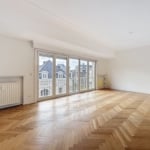 Salon lumineux avec parquet en chevrons, grandes baies vitrées et vue sur balcon.