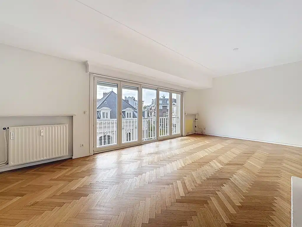 Lichte woonkamer met houten vloer en uitzicht naar buiten Woonkamer - Brugmannplein - 2 slaapkamer appartement - Elsene