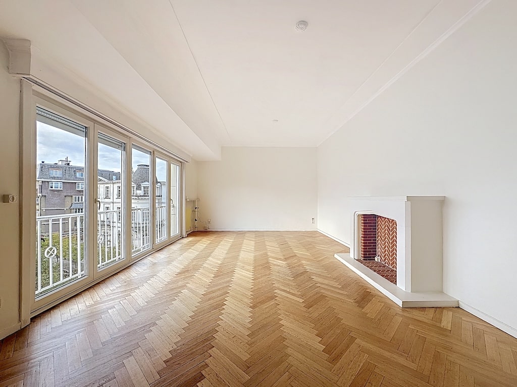 Salon minimaliste lumineux avec cheminée moderne, parquet en chevrons et grandes fenêtres.