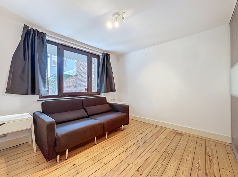 Salon moderne et minimaliste avec canapé sombre, grande fenêtre et ambiance chaleureuse.