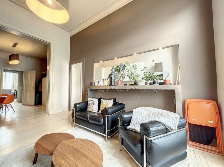 Salon contemporain élégant avec fauteuils en cuir, plantes, éclairage moderne et espace lumineux.