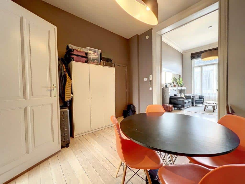 Salon moderne lumineux avec table ronde noire, chaises orange et espace ouverte accueillant.