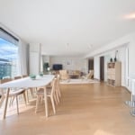 Salon lumineux avec mobilier moderne, cuisine ouverte, grande table, vue naturelle et décoration épurée.