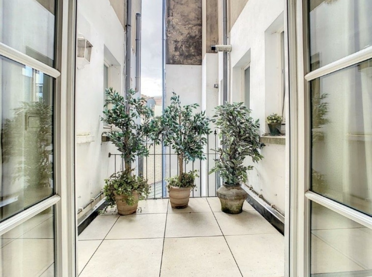 Balcon lumineux avec plantes vertes, railing en fer forgé et vue urbaine apaisante.