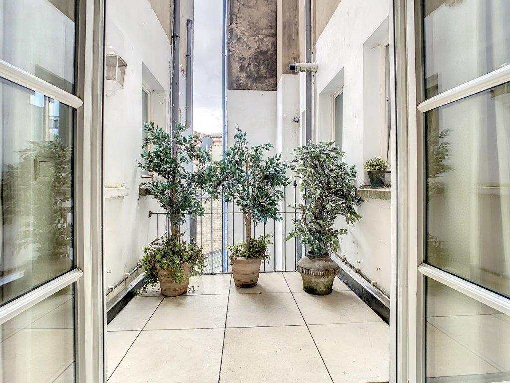 Balcon lumineux avec plantes vertes, railing en fer forgé et vue urbaine apaisante.