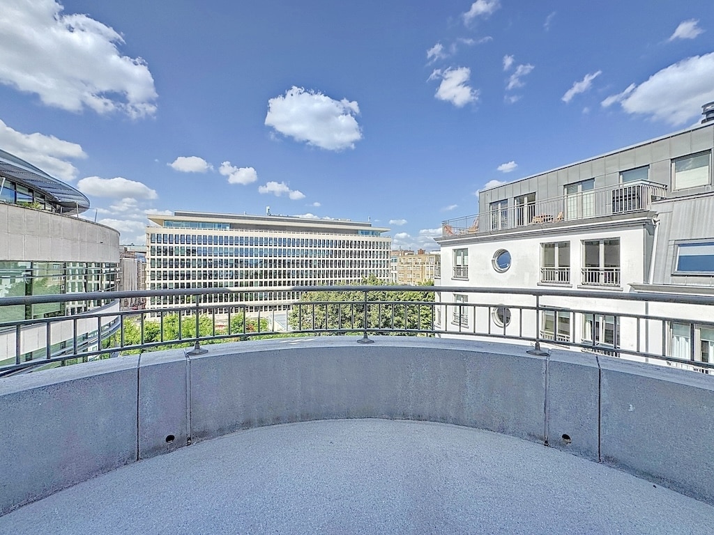 Balcon moderne avec vue urbaine, ciel bleu, espace détente, architecture contemporaine et verdure.
