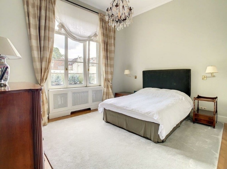 Chambre élégante et lumineuse avec murs verts pastel, lit blanc, bois et fenêtres à rideaux.