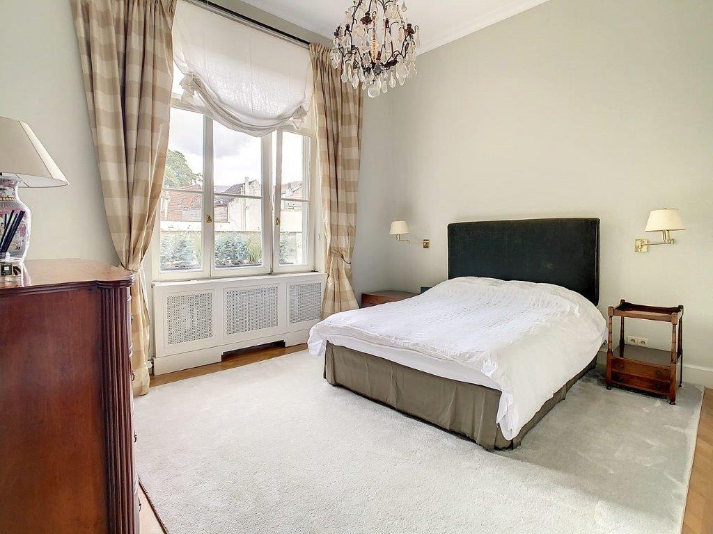 Chambre élégante et lumineuse avec murs verts pastel, lit blanc, bois et fenêtres à rideaux.