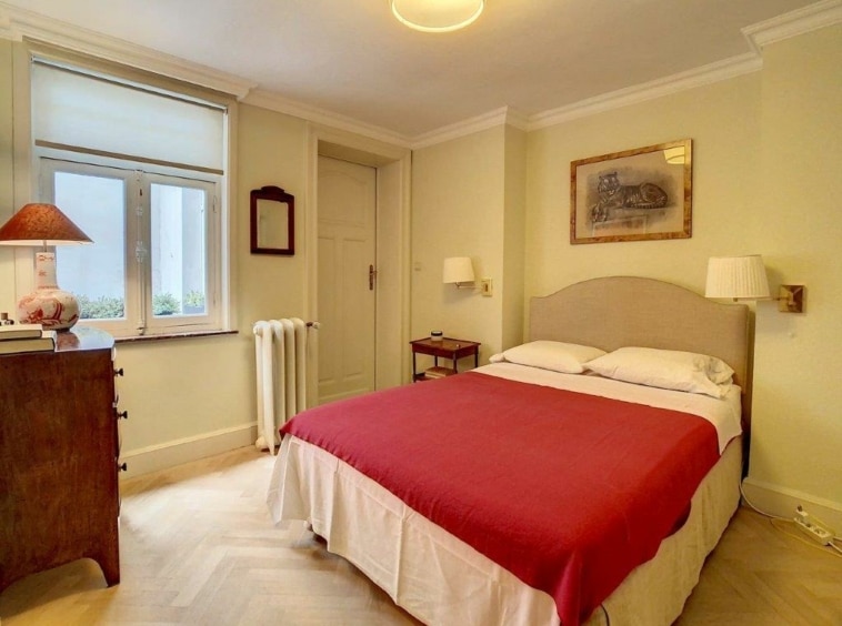 Chambre vintage chaleureuse avec lit rouge, lumière naturelle, meubles en bois et ambiance relaxante.