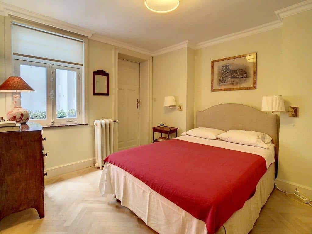 Chambre vintage chaleureuse avec lit rouge, lumière naturelle, meubles en bois et ambiance relaxante.