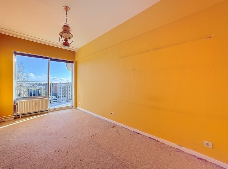 Chambre lumineuse aux murs jaunes, grande fenêtre, volets blancs, plafond avec ventilateur rustique.