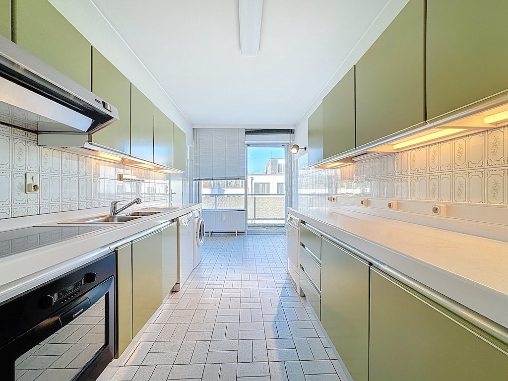 Cuisine moderne aux murs olive, éclairage doux, vue urbaine et sol en carreaux élégants.