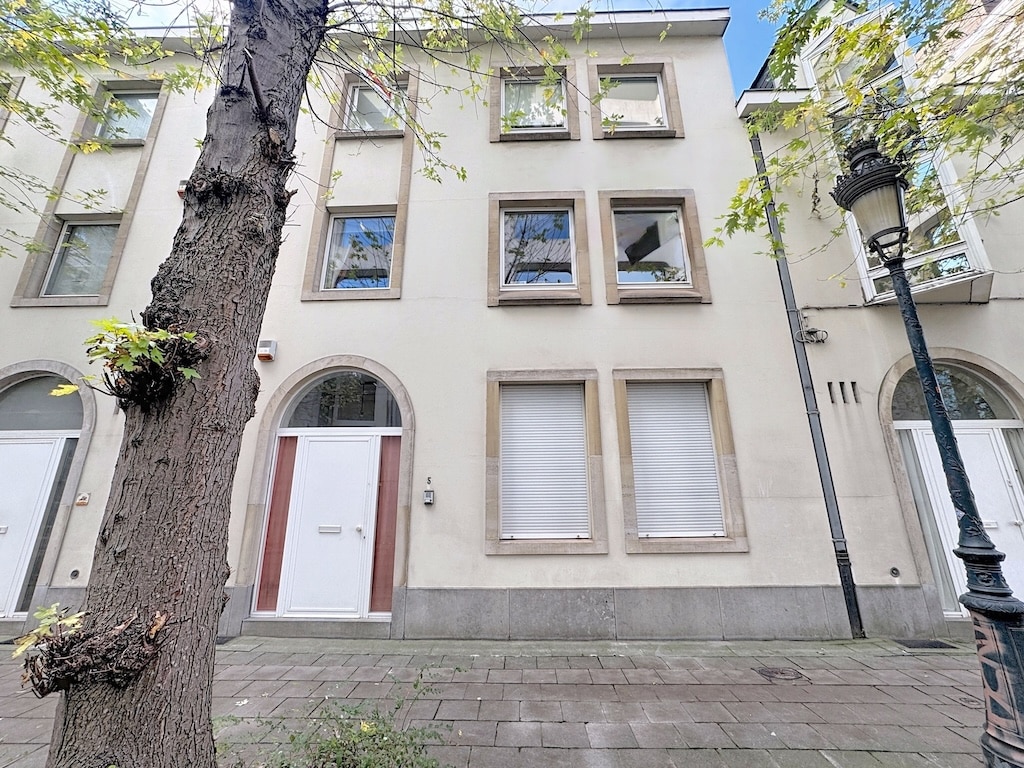 Façade dimmeuble moderne avec arbre ancien, lampadaire vintage, sous ciel clair.