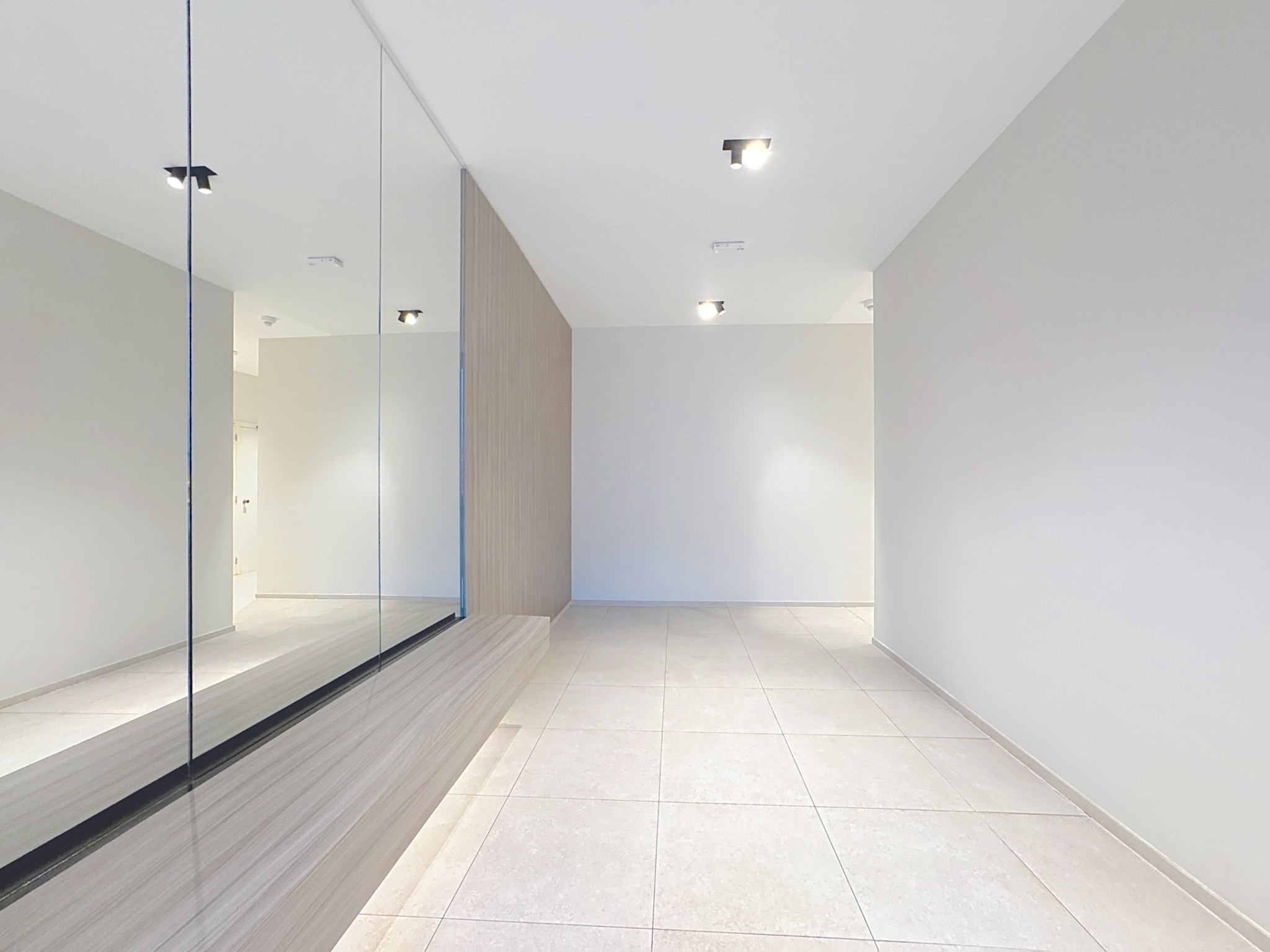 Espace intérieur moderne minimaliste avec miroir, sol clair, éclairage encastré, ambiance lumineuse.