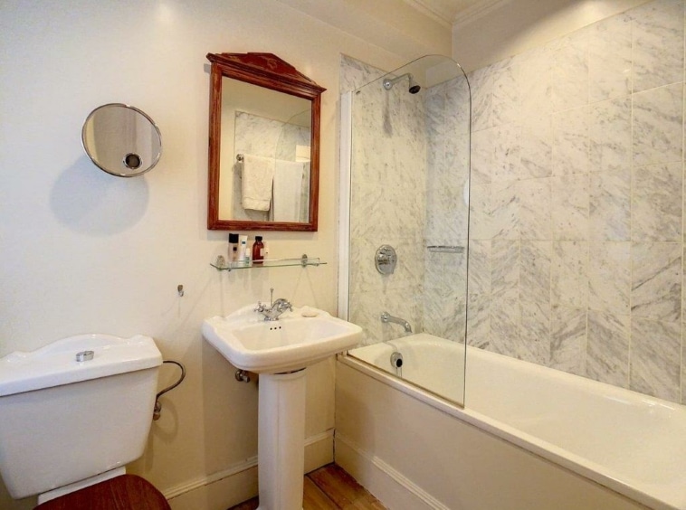 Salle de bain moderne avec marbre, lavabo sur pied, miroir rond, et douche en verre.