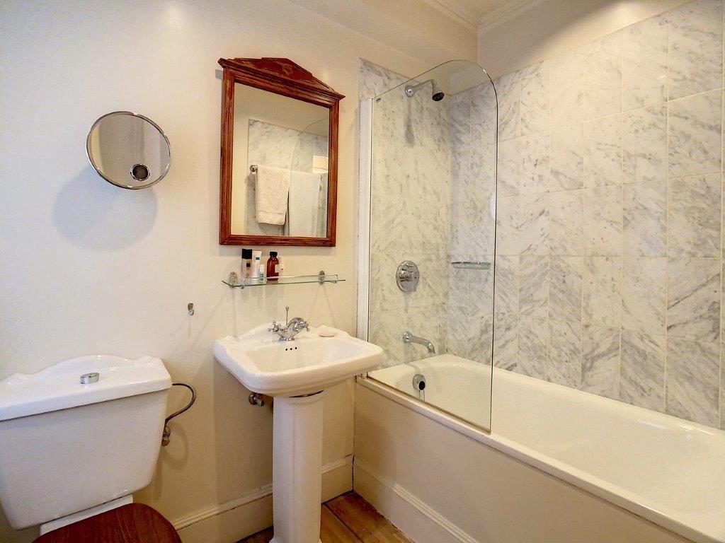 Salle de bain moderne avec marbre, lavabo sur pied, miroir rond, et douche en verre.