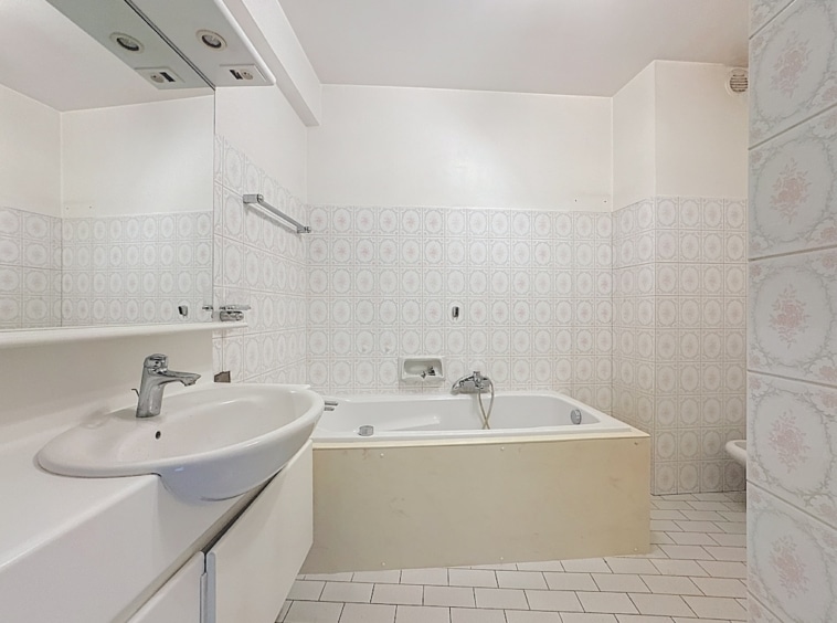 Salle de bain moderne avec baignoire en coin, grand miroir et design épuré.