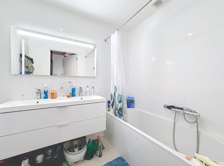 Salle de bain moderne avec baignoire blanche, miroir rétroéclairé et accessoires colorés.