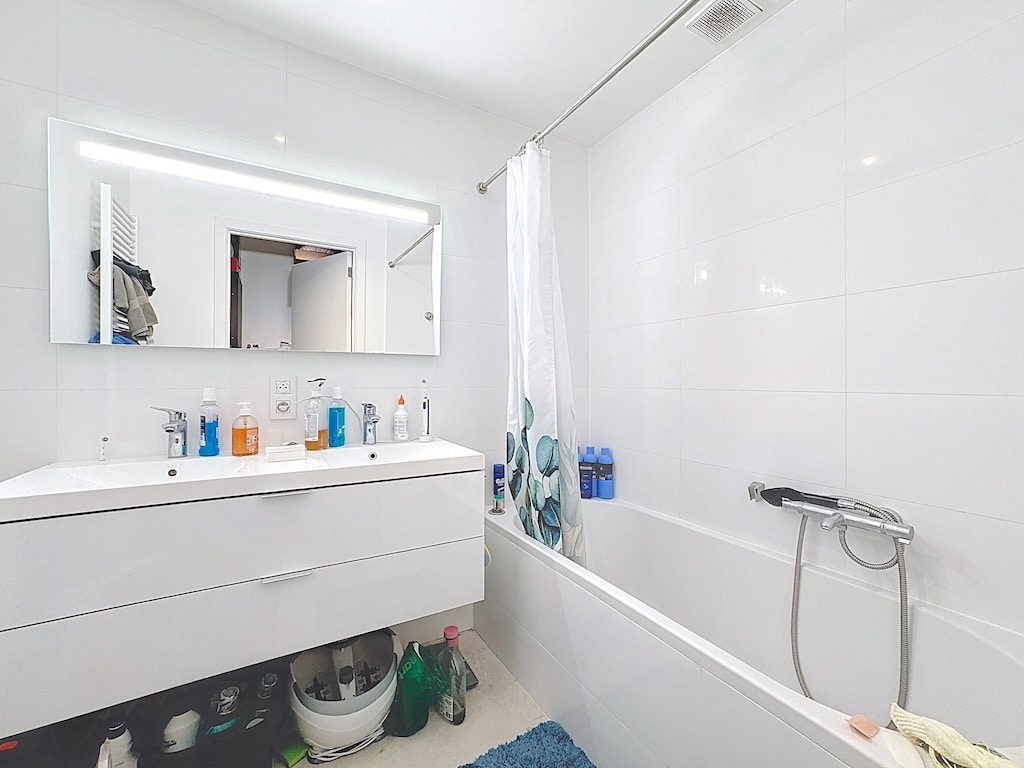 Salle de bain moderne avec baignoire blanche, miroir rétroéclairé et accessoires colorés.