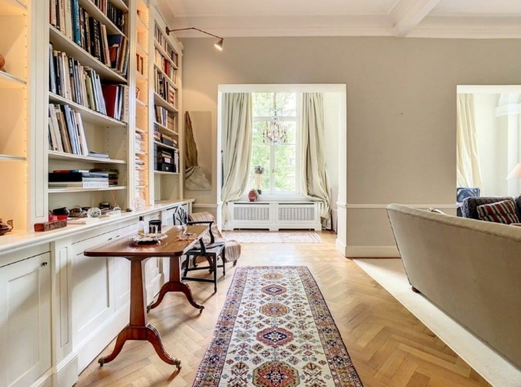 Salon lumineux avec parquet en chevrons, bibliothèque, canapé moderne et décoration chaleureuse.
