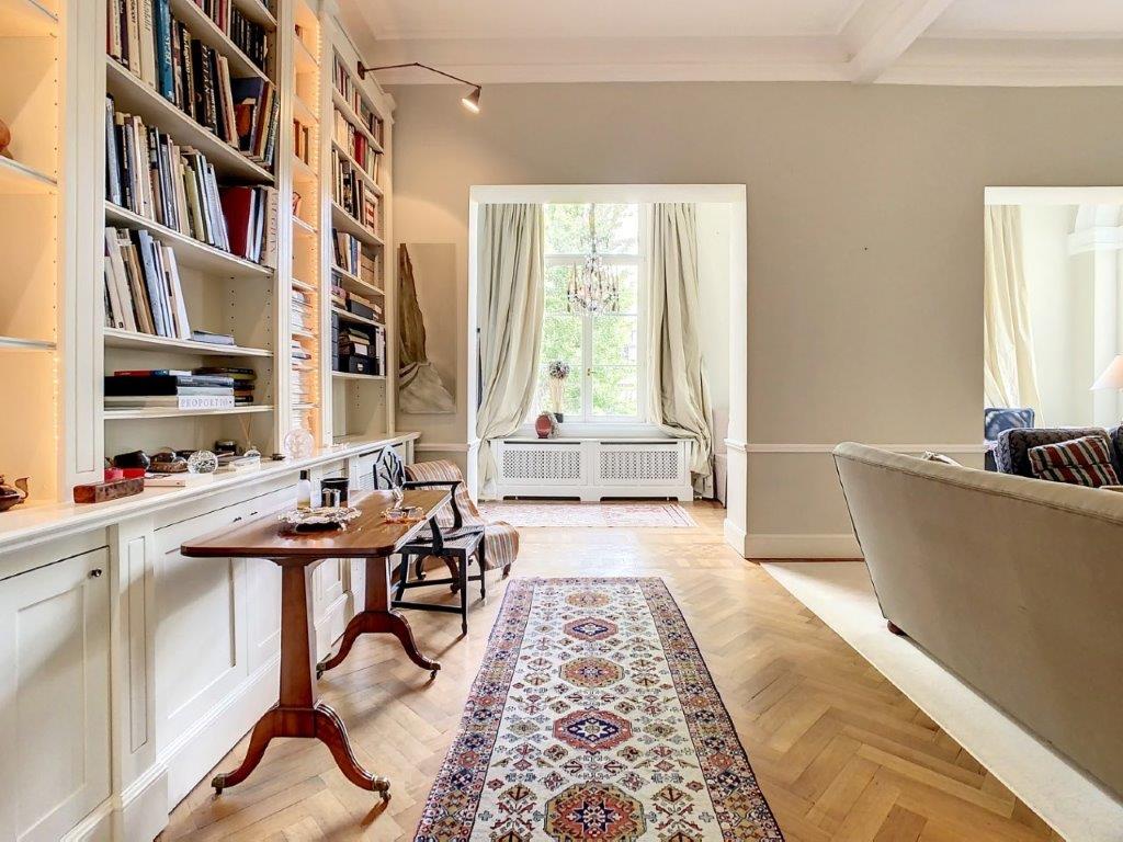 Salon lumineux avec parquet en chevrons, bibliothèque, canapé moderne et décoration chaleureuse.